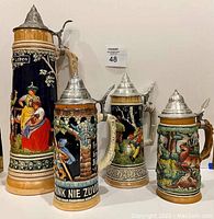 Front view of all four German steins side-by-side showing detailed scenes and pewter lids