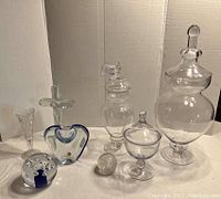 Photo showing all glass decor items together: three Jardinair jars with stoppers of different sizes, glass cross, heart-shaped vase, two glass globes, and short vase/goblet.