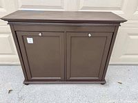 Front facing view of wooden hamper with two doors and silver knobs.