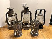 Front photo of all five items: three metal kerosene lanterns and two tin candle holders with glass inserts