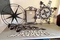 Photo showing all metal wall art pieces and candle holders displayed on table against wall, includes compass, star, off white art, photo frame, and candle holders.