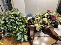 Wide view of assorted artificial greenery including ferns, leaves, and floral arrangements with wood planters laid on a table.