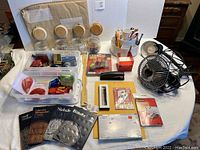 Photo showing the entire assortment of office supplies on table, including clip-on fan, clip-on light, rotating organizer with utensils, clear containers, tape dispensers, stapler, stamps, and envelopes.