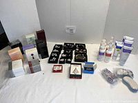 Photo of overall lot showing Avon boxed perfumes, jewelry pieces in boxes including bracelets, necklaces, pins, and packaged skin and foot care products with pumice bars.