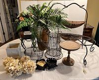 Overview of all items showing two-tier basket, African vase with fern, plant stands, flower arrangements, and candle holders.