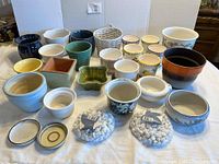 Wide view showing assortment of various small plant pots, some with colorful glazes and designs, two bags of white decorative rocks, and several saucers.