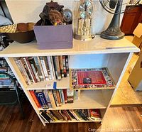 Full front view of white bookcase containing multiple books, a purple box, and decorative items on top (not included).