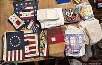 Wide view of various folded cloth napkins and linens with American flag pattern and other designs, also showing some napkin rings in a small basket