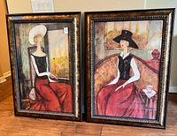 Two framed paintings of European fashion ladies placed side by side on floor.