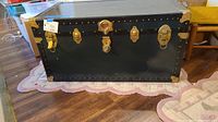 Front view of vintage black metal trunk showing brass locks and corner protectors.