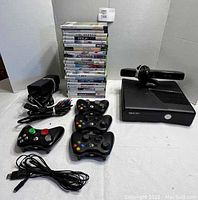 Wide shot showing Xbox 360 console, Kinect sensor, 4 controllers, AV cable, USB cable, and stacked games.