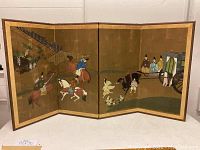 Full view of four-panel Japanese folding screen showing painted scene of riders, horses, attendants, and carriage on gold background.