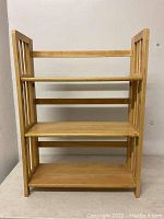 Front view of a wooden folding bookshelf with three shelves and vertical slats on the sides.