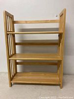 Front view of the folding wooden bookshelf showing three shelves and vertical slat sides.