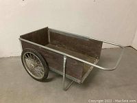 Side angle showing full side profile, large spoked rubber wheel, solid wooden box, galvanized metal frame, and handle.