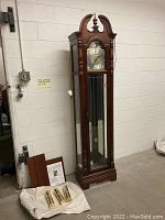 Front view of clock showing wooden case, glass door and loose panels on floor