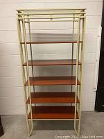 Front view of tall metal framed etagere with five cherry wood shelves and cream-colored metal frame.