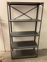 Front view of the gray metal shelving unit with five shelves against a white wall.