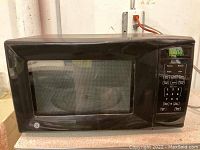 Front view of the black GE microwave, showing the door with glass window, digital green LED display, and control panel with numeric keypad and function buttons.