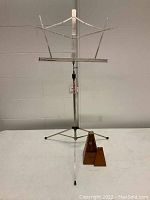 Photo of the metal telescoping music stand standing upright with tripod base and a wooden metronome placed nearby.