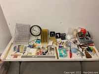 Full overview of the items including clock, rulers, small tools, and bins of hardware on white folding table in front of white wall