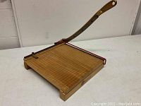 Overall view of the paper cutter showing the wooden base with grid and long wooden cutting arm.