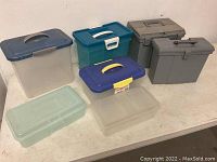 View of all seven plastic storage containers including file totes and lidded bins arranged on a white table against a wall.