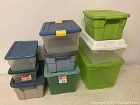Stacked assorted plastic bins with lids in various sizes and colors on table against wall