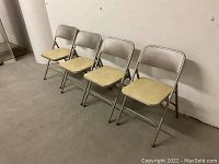 Four metal folding chairs aligned side by side showing cream padded seats