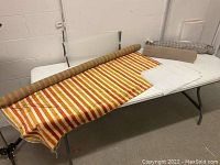Image showing full view of vintage striped upholstery fabric roll spread on table with cushioned shelf liner and rolled fabric