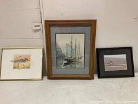 Three framed artworks: two sandpiper themed and one ship themed, shown together on the floor against a wall