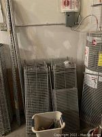 Photo showing stacked metal wire shelves, wall mount bars next to a water heater and a bin on the floor