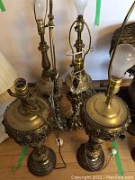 Photo showing six vintage brass lamps grouped together, highlighting varied designs of bases and harp fittings for shades.