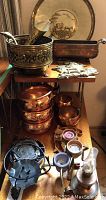 Display of various brass and copper decor including pots, bowls, candle holders, and trays arranged on metal and wooden shelving units.