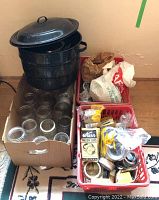 Wide view showing black enamel canning pot with lid, box of glass canning jars, and baskets with lids and rings.
