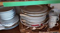 Multiple stacks of white plates and bowls with floral pattern cups in cabinet