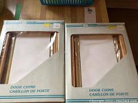 Two Norlite door chimes in original packaging, front view showing product through clear windows.