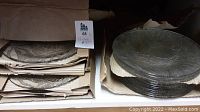 Glass plates stacked and packed in cardboard boxes showing pattern details and quantity.