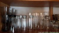 Clear tall and short drinking glasses along with some upside down glasses on a wooden shelf.