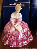 Front view of seated figure in pink floral gown holding fan