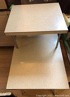 Photo of two laminate side tables showing the light-colored textured laminate surface and metal legs, with one table placed on top of the other.