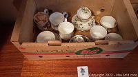 Wooden box containing various Royal Albert teacups and some saucers, arranged loosely, showing some saucers missing.