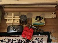 Overall view of the vintage kitchen items laid out including wrapping paper stand, scale, tin box, egg beater, red egg mold, and grater.
