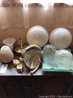 Full lot on a wooden surface including large and small glass globes, brass bases, and various shaped lamp shades.