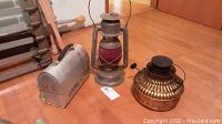 Photo of two vintage kerosene lamps and one metal lunch pail on wood floor, showing overall items in lot.
