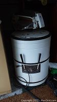 Front view of vintage Kenmore round washing machine showing control panel, power cord, and attached hose.