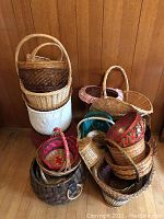 Photo showing stacked wicker baskets in various colors and sizes, some with handles, arranged on the floor in front of wood paneling wall.
