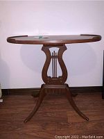 Front view of wood oval accent table with lyre-shaped base, showing curved legs and medium brown finish.