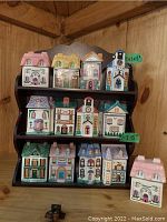 Front view of wooden rack with ceramic spice jars shaped like houses arranged on three shelves.