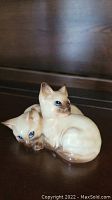 Front and right side view of Beswick two cats figurine showing blue eyes, cream color with brown shading, sitting position, minor chip on ear visible